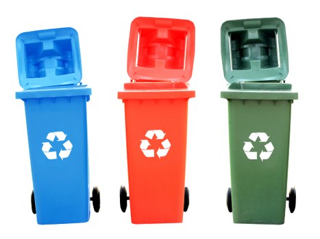 This image displays three upright wheeled rubbish bins positioned side by side, each with a closed lid. The first bin on the left is blue and features a white recycling symbol on its front face, indicating its use for recyclable waste. The middle bin is red with a similar white recycling emblem, typically used for general waste or specific waste categories in waste management services. The third bin on the right is green, also with a white recycling icon, commonly associated with compost or organic waste collection. The bins are made of durable plastic with textured surface patterns and have black plastic wheels attached at the base, facilitating easy movement. They are set against a plain white background, with no visible environment or surroundings, focusing solely on the bins themselves. The image suggests a professional waste collection or recycling arrangement, relevant to rubbish removal services as provided by companies like Commercial Waste Holborn in London, within the postcode area associated with the Holborn district.